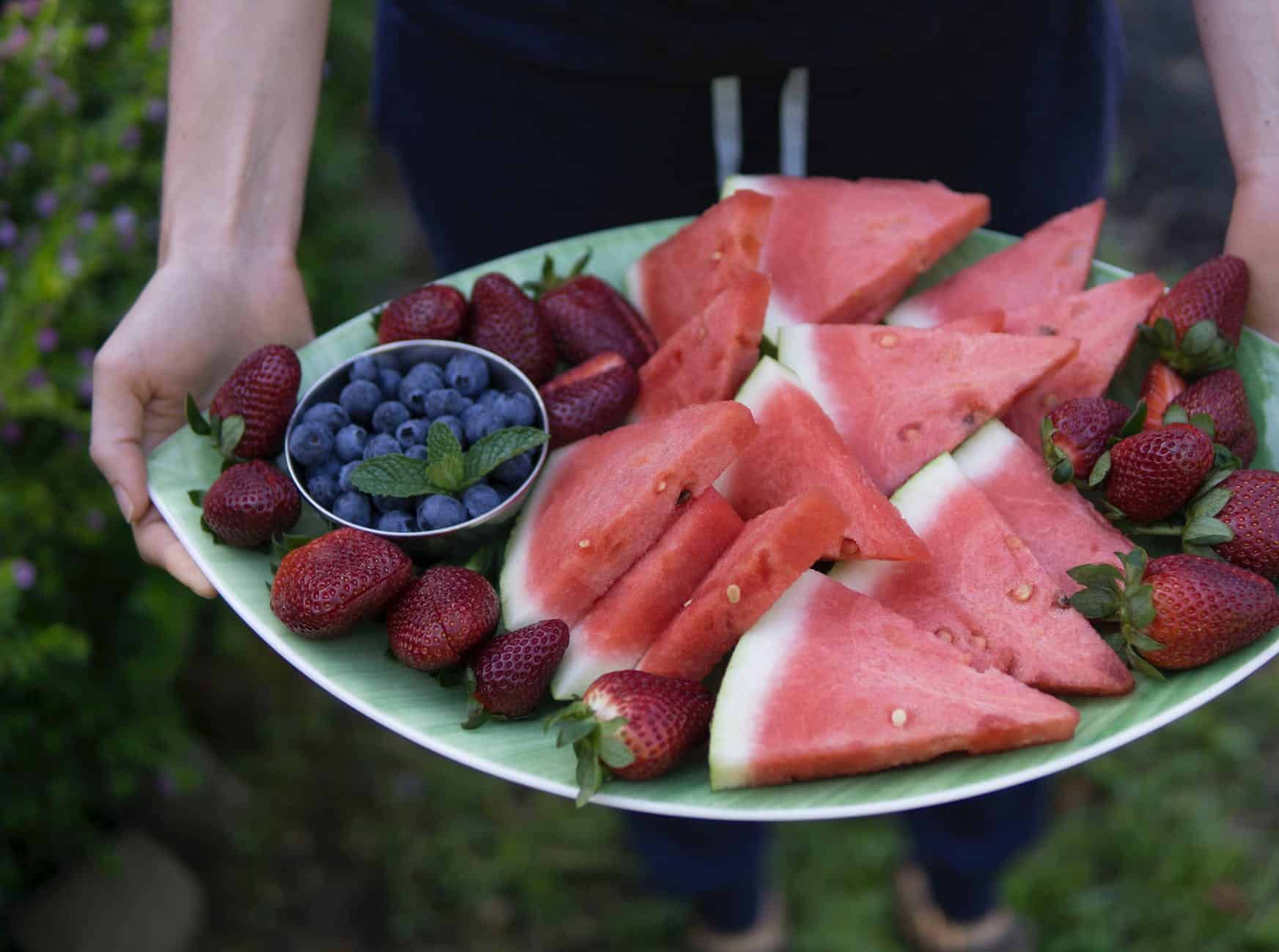 Eine Person mit einem großen Snackbrett mit Früchten wie Erdbeeren, Blaubeeren und Wassermelone